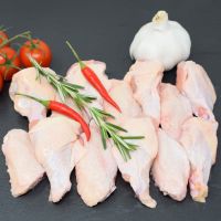 Raw chicken wings arranged on a dark surface with rosemary, red chilies, tomatoes and garlic.